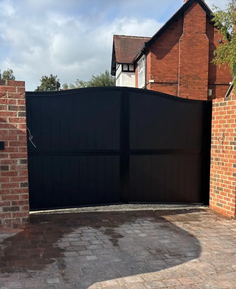 Black boarded electric gates with a shaped ogee top, between red brick piers at a period house