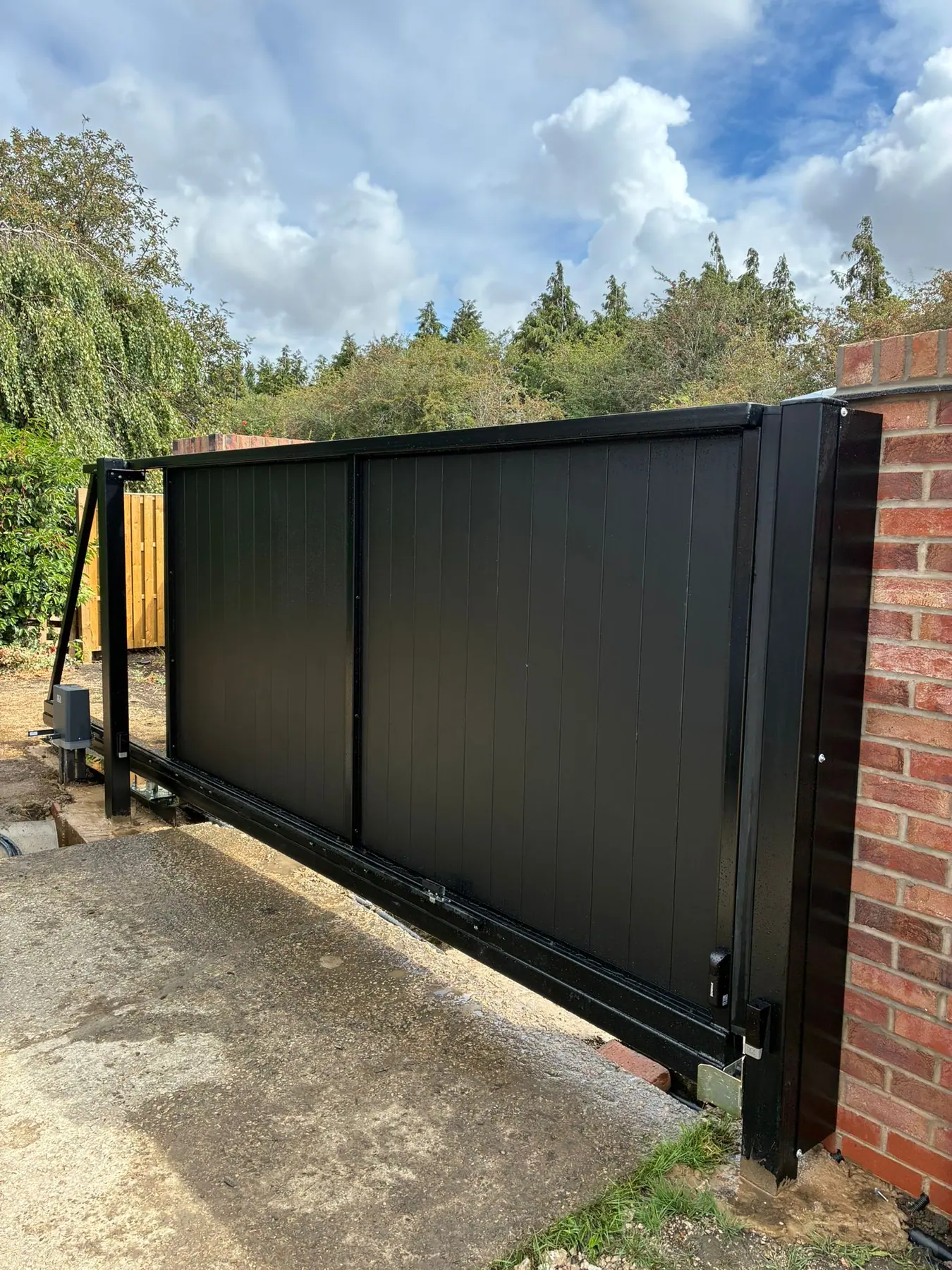 Black boarded electric sliding gate on its track, between red brick piers