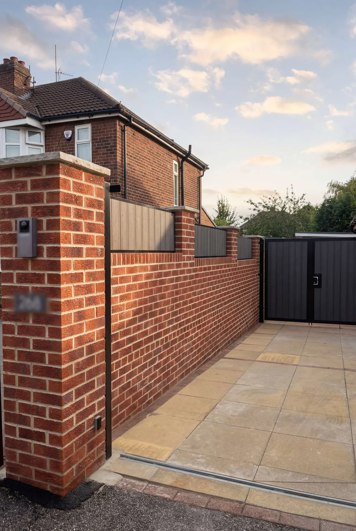 Dark electric gate set into a red brick boundary wall with an intercom