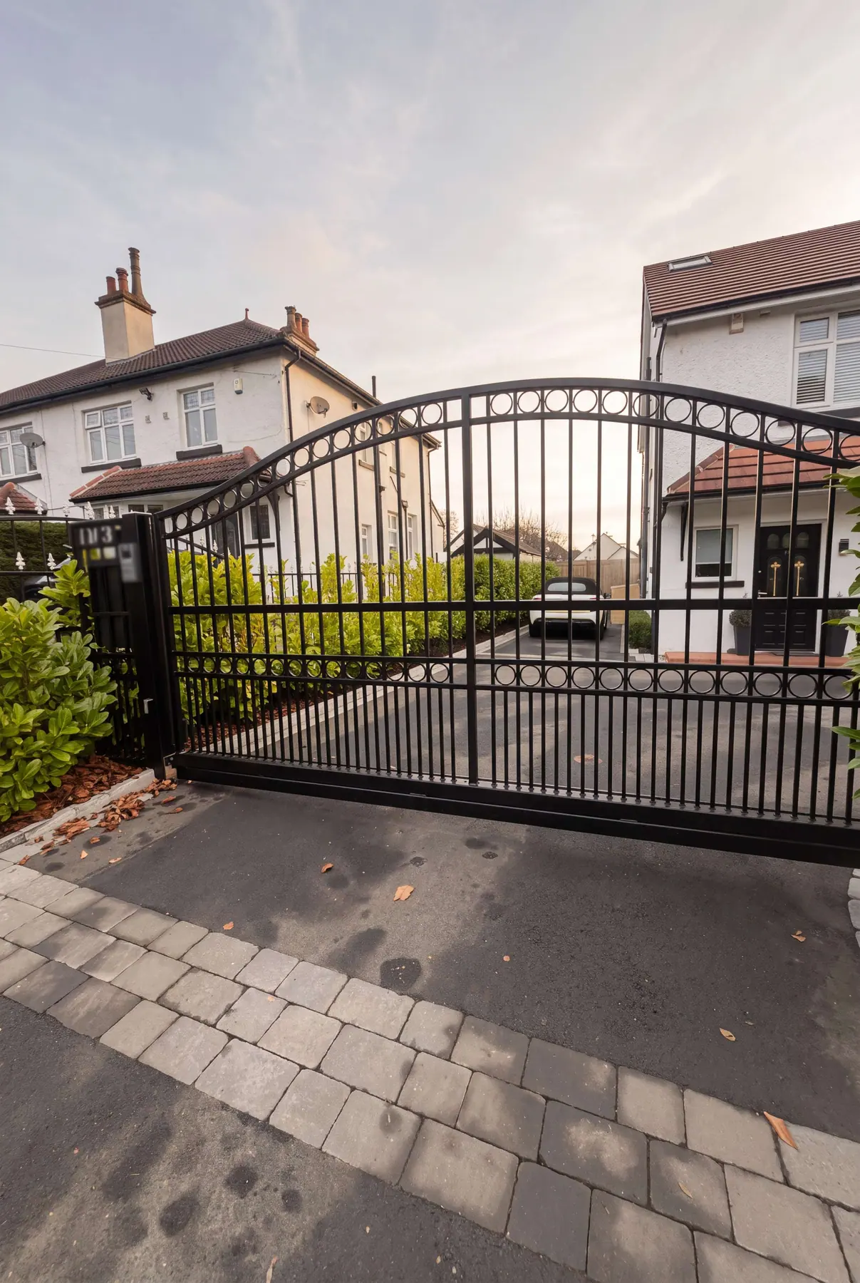 Arched wrought iron electric gates at a cream rendered house