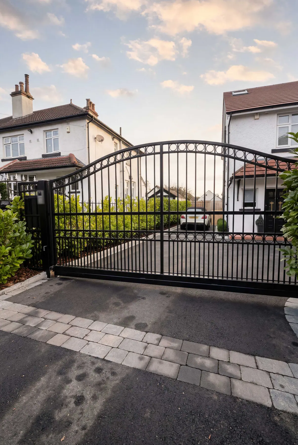 Arched wrought iron electric gates at a cream rendered house