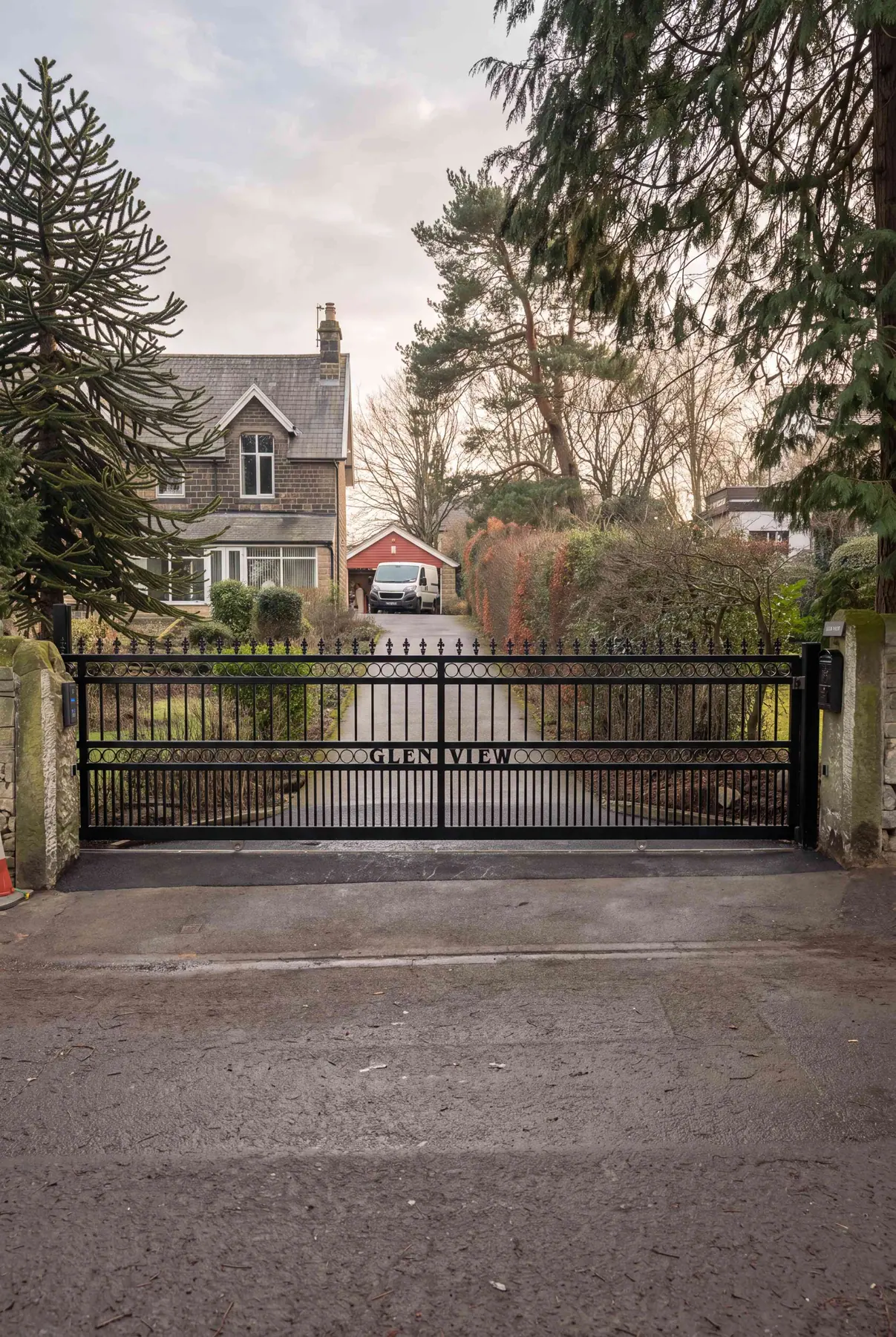 Wrought iron electric gates at a stone house with mature planting