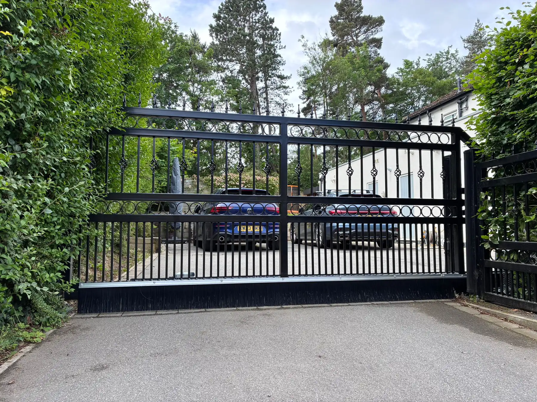 Black wrought iron electric gates with ring detailing and matching railings, on a tarmac driveway