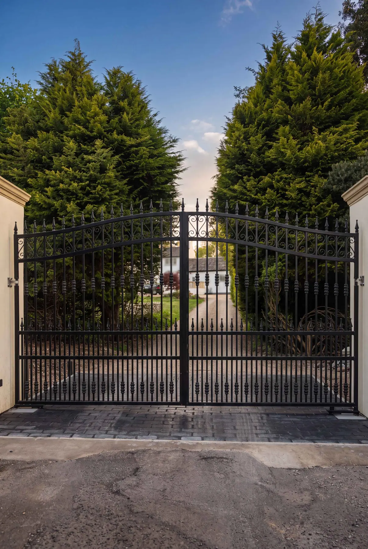 Tall ornate wrought iron electric gates framed by clipped hedges