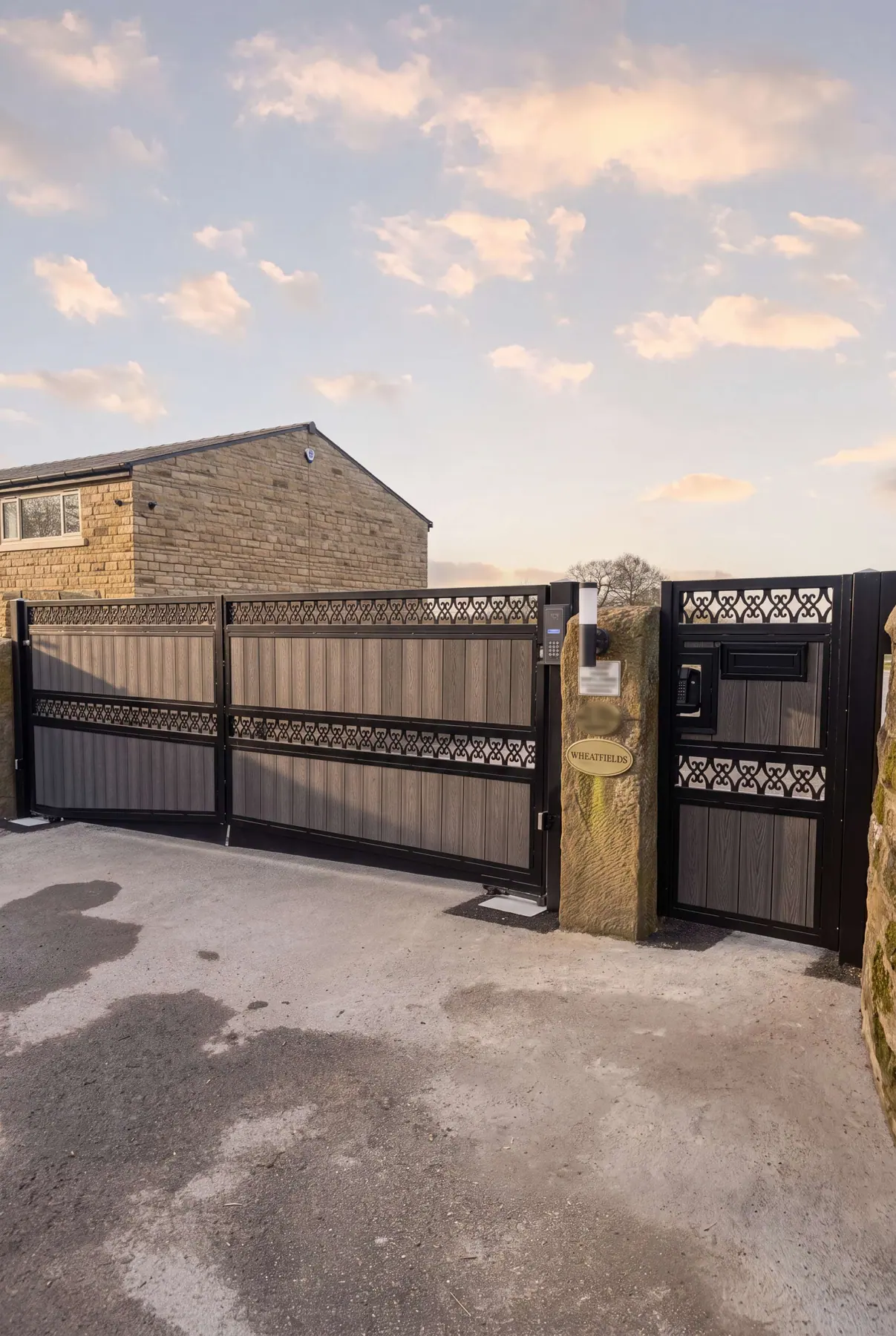 Dark electric gate with a decorative lattice band, set between stone pillars