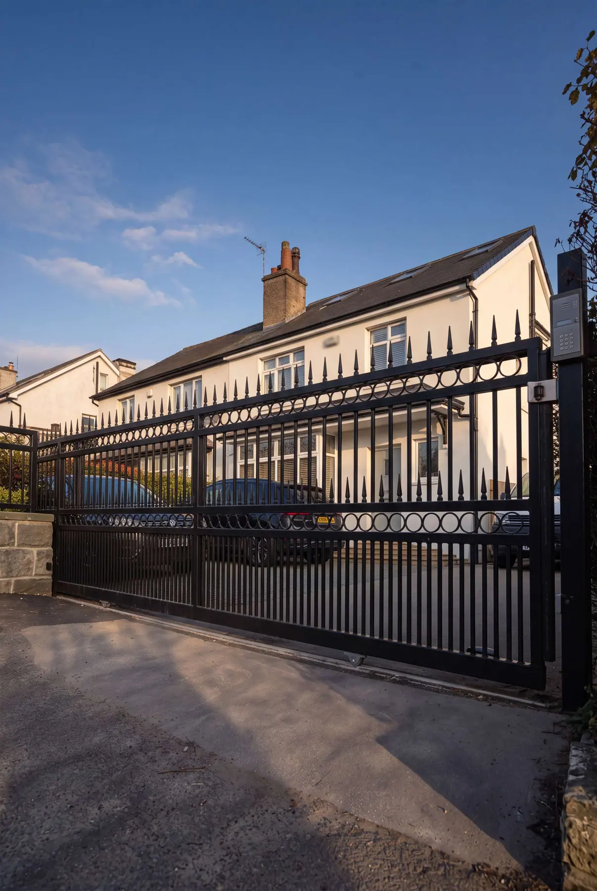Black electric gates with matching ring-detail railings outside white rendered houses