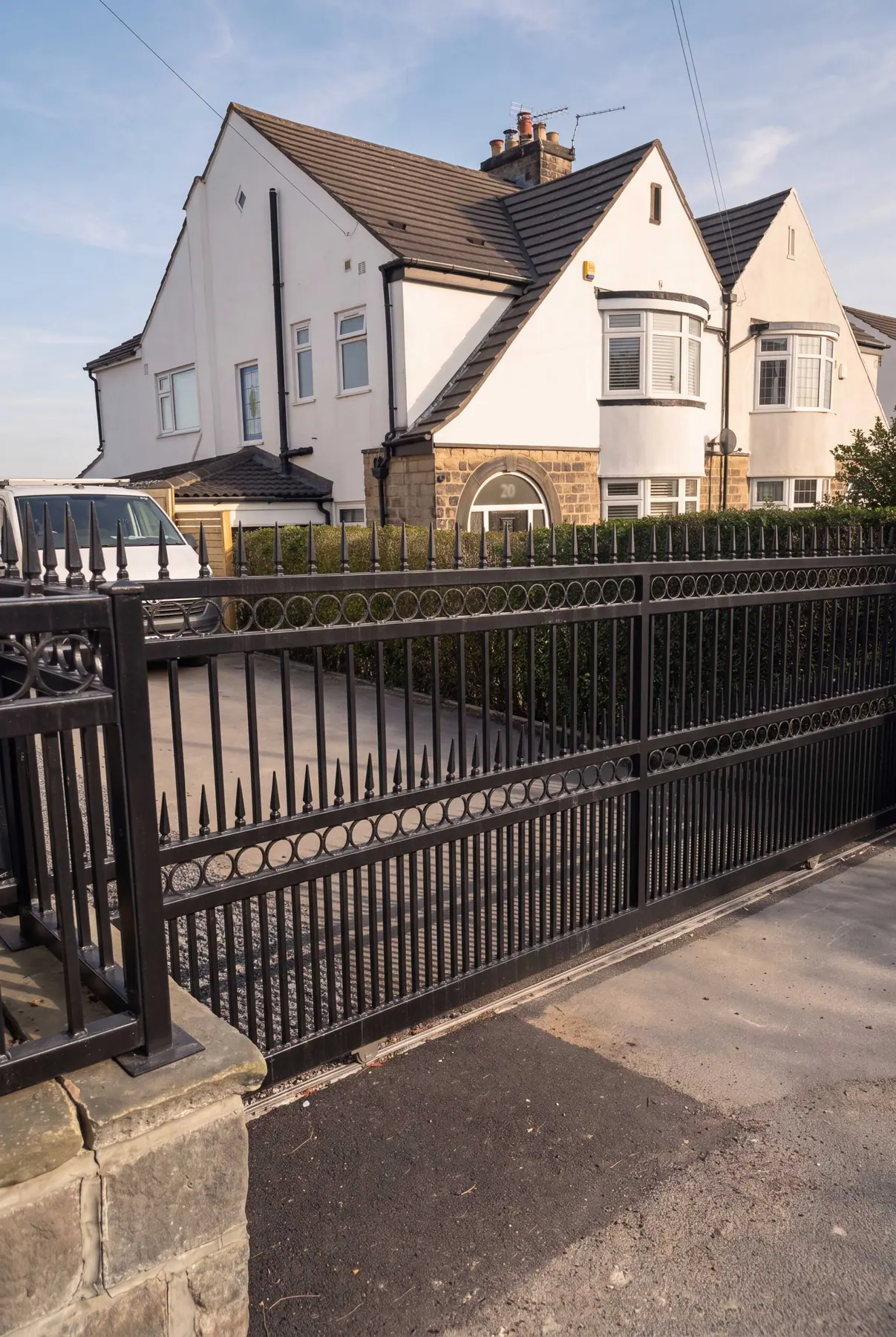 Black electric gates with matching ring-detail railings outside white rendered houses