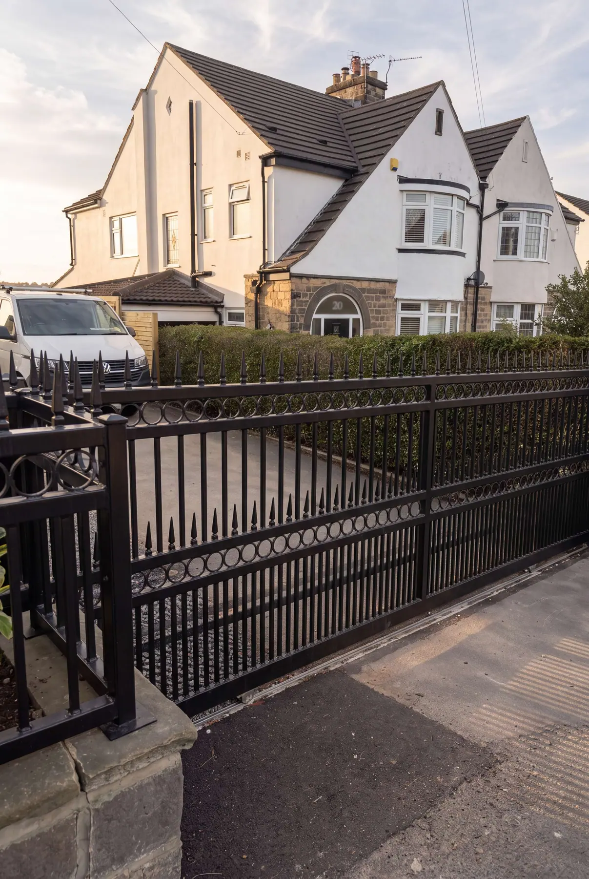 Black electric gates with matching ring-detail railings outside white rendered houses
