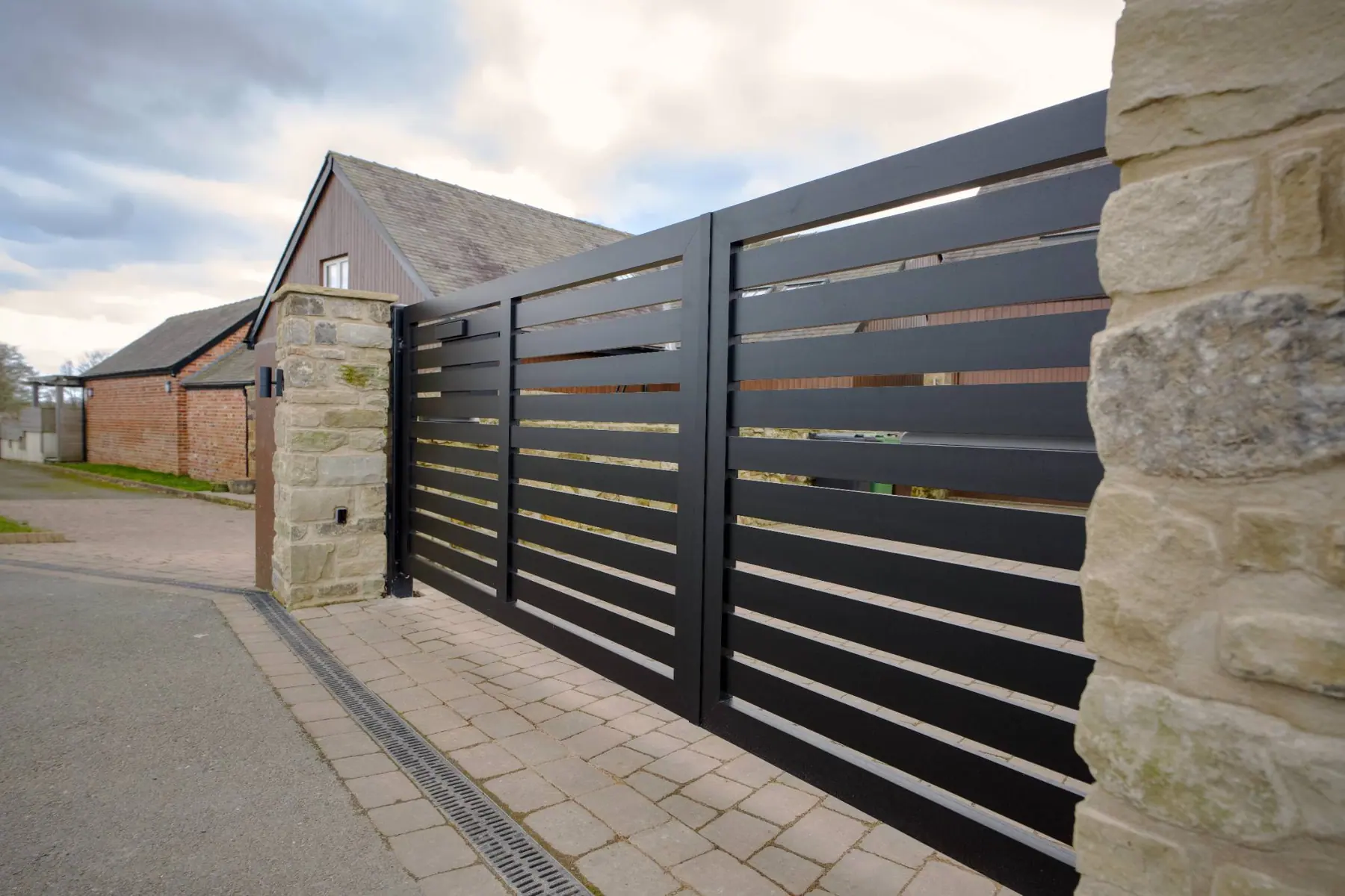 Black horizontal-slat electric sliding gate on a stone-pillared driveway