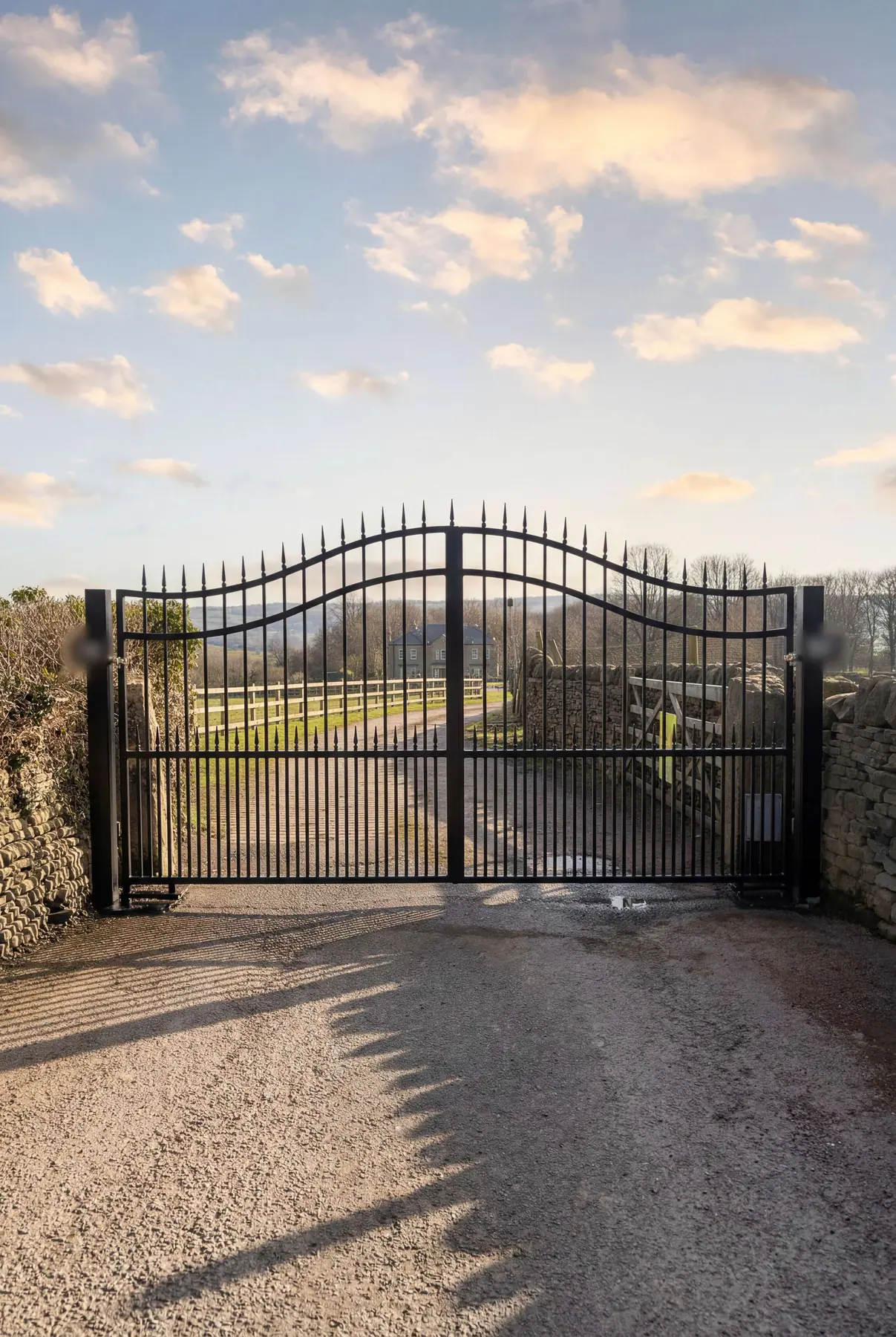 Arched wrought iron manual gates opening onto open countryside