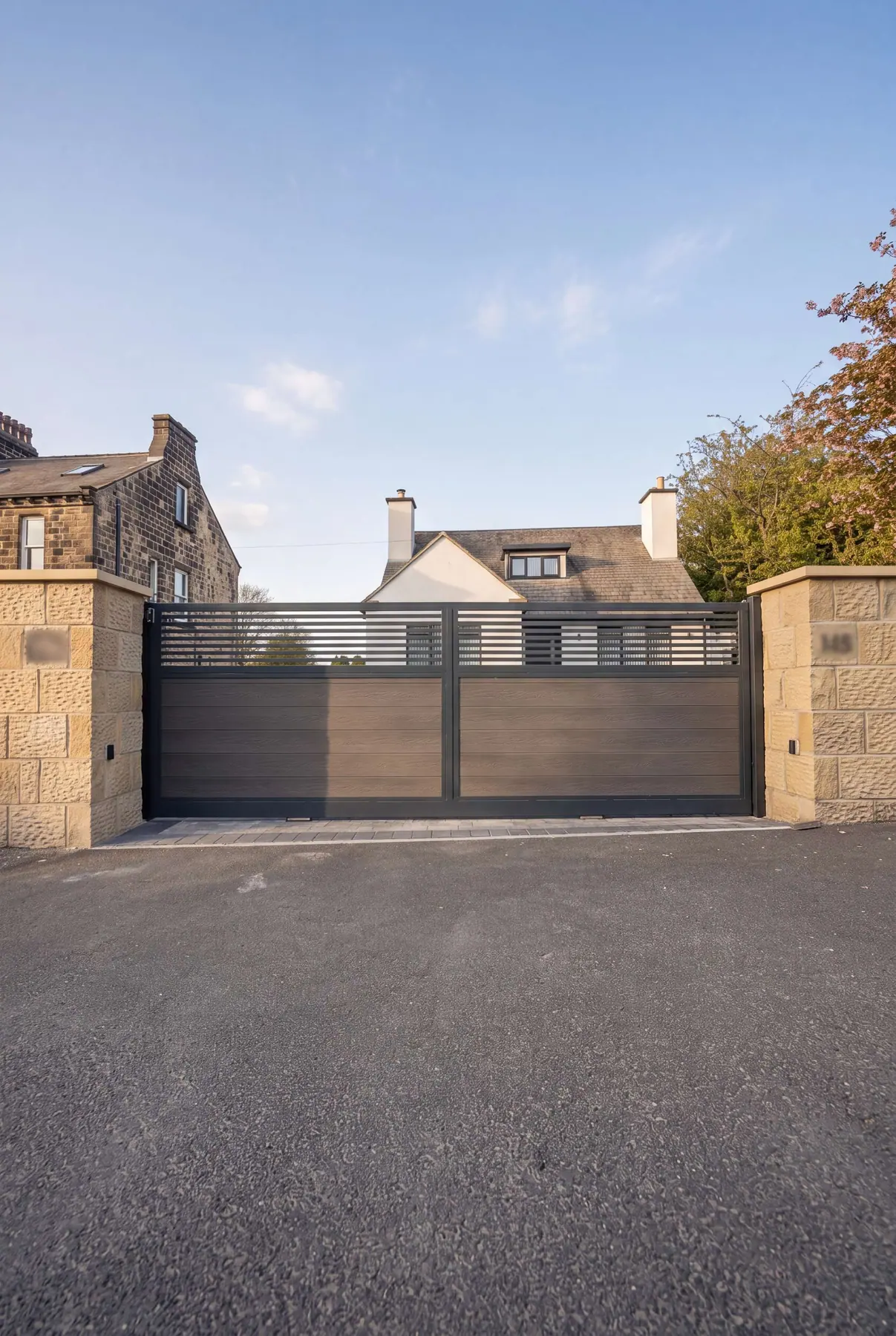 Composite driveway gates with a slatted top panel, between sandstone pillars at a Yorkshire home